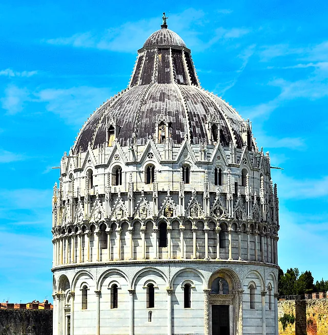 The Baptistery of Pisa, a round white marble building with a ribbed dome and Gothic pinnacles, against a bright blue sky