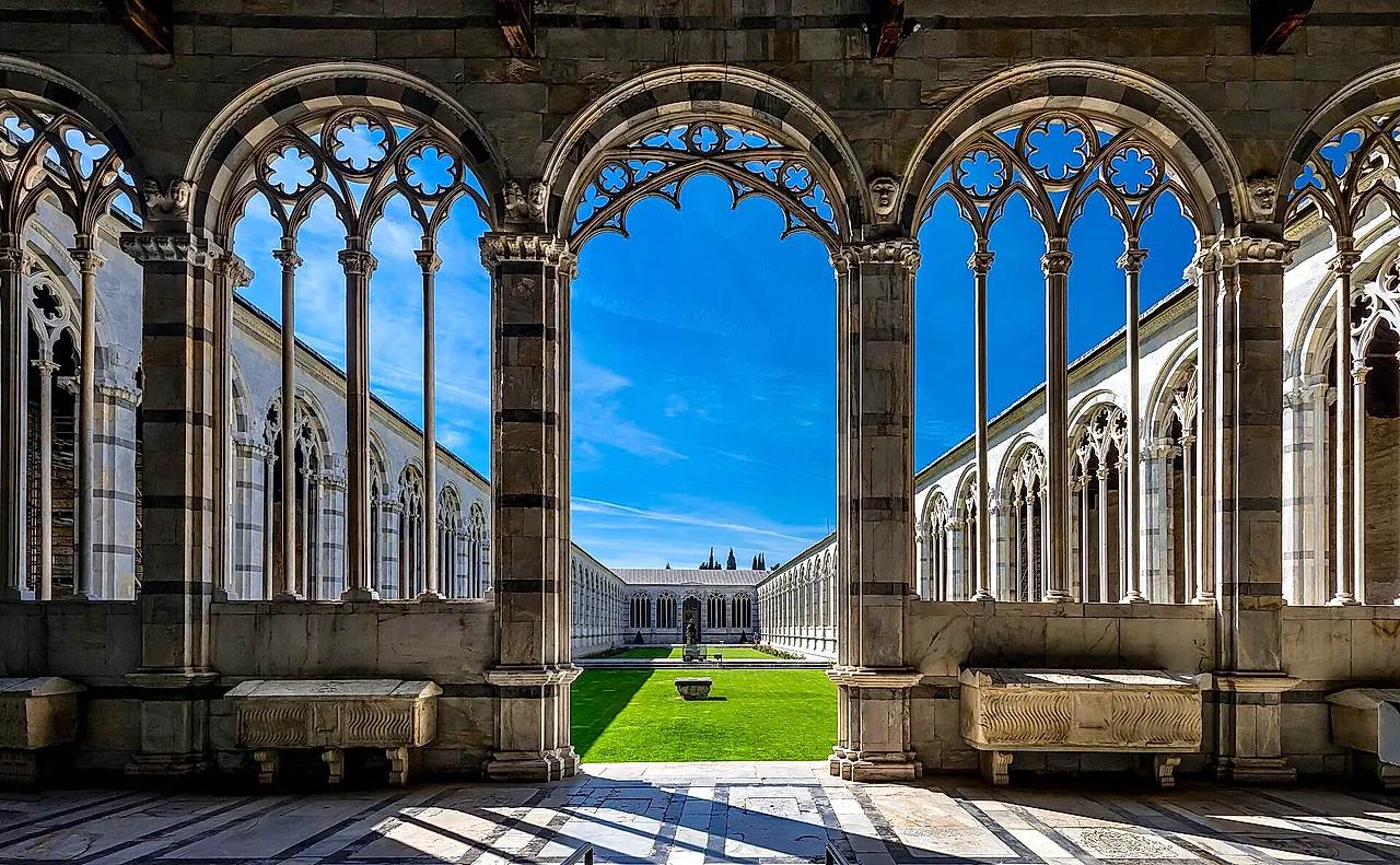 Gothic arches of the Camposanto Monumentale framing the green courtyard in the sun