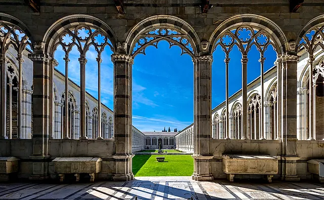 Gothic arches of the Camposanto Monumentale framing the green courtyard in the sun