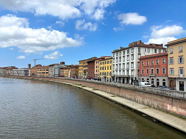 The Lungarno in Pisa: the Arno curving along a row of pastel-coloured buildings under a sky with clouds