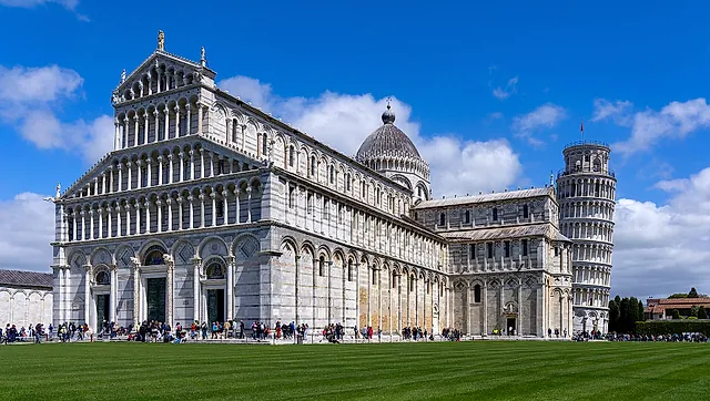 The façade of Pisa Cathedral with its tiers of white and grey marble arches and the Leaning Tower on the right, on the lawn of Piazza dei Miracoli