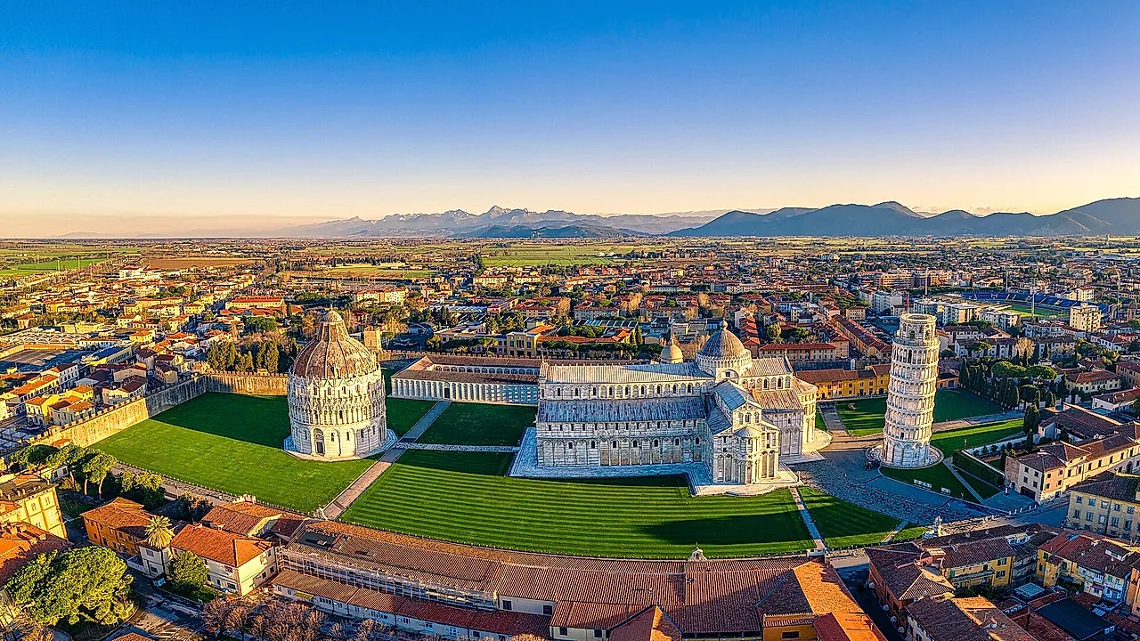 Aerial view of Piazza dei Miracoli: the Baptistery, the Cathedral and the Leaning Tower on their green lawn, with the roofs of Pisa and the hills beyond