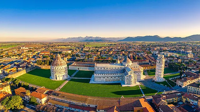 Aerial view of Piazza dei Miracoli: the Baptistery, the Cathedral and the Leaning Tower on their green lawn, with the roofs of Pisa and the hills beyond