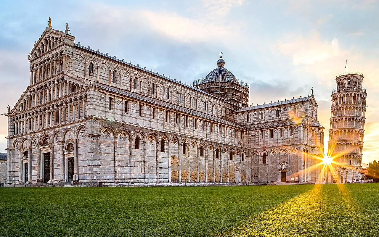 Pisa Cathedral at sunrise: the long marble façade with the sun flaring behind the Leaning Tower on the right