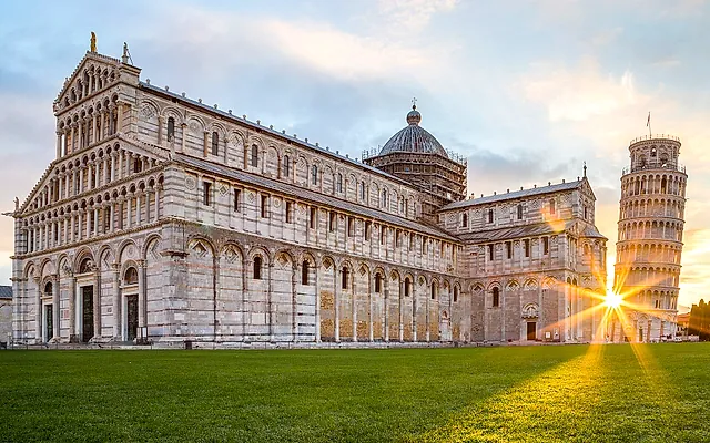 Pisa Cathedral at sunrise: the long marble façade with the sun flaring behind the Leaning Tower on the right