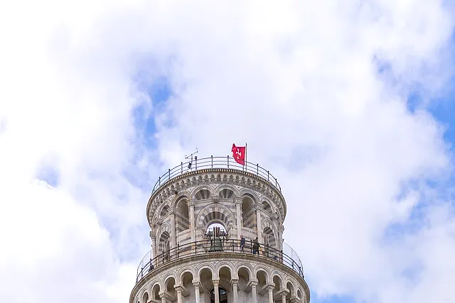 The Leaning Tower of Pisa seen from below, its tiers of arches leaning to one side under a cloudy sky