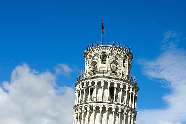 The Leaning Tower of Pisa from the foot of the lawn: white marble tiers of columns leaning against a blue sky with clouds